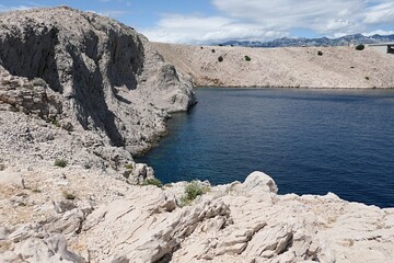 Arid coastal rocky bay medieval Fortica fortress and Pag Bridge, Zadar county, Northern Dalmatia, Croatia. Deep blue bay water with some ripples visible. Summer daylight sunshine. 