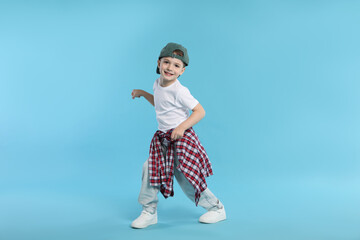 Happy little boy in baseball hat dancing on light blue background