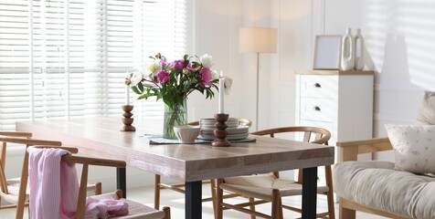 Dining table with beautiful flowers and dishware in room. Interior design