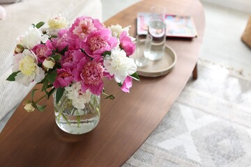 Bouquet of beautiful peonies and water on coffee table indoors. Interior design