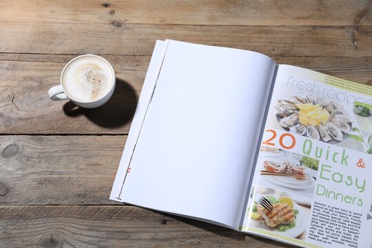 Open magazine and coffee on wooden background. Mockup for design
