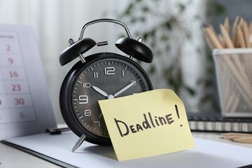 Sticky note with word Deadline, alarm clock, stationery and calendar on table indoors, closeup
