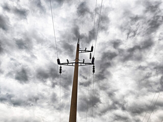 A towering wooden utility pole rises against a backdrop of a dramatic sky, where dark, swirling...