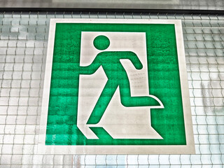 Emergency exit sign mounted on a glass wall indicating a safe path to follow in case of an emergency