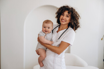 Visit of cute little girl, holding her in hands. Female doctor is with newborn baby indoors