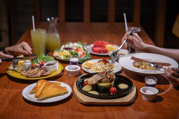 Hands are using a spoon and knife for eating steak and spaghetti, enjoying the meal.