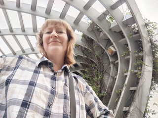 Mature woman enjoying a selfie at an outdoor structure during a travel excursion in a lush...