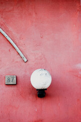 White round lamp with metal pipe complementing house number eighty seven against vibrant red wall,...
