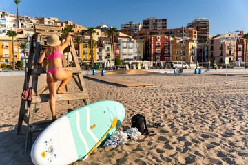 Lifeguard climbing watchtower on beach with paddle board