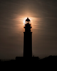 Stunning silhouette of a tall lighthouse against the sun.