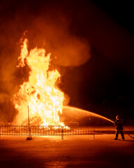 Brave firefighter extinguishing a large raging bonfire at night.