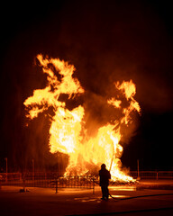 Silhouette of a firefighter standing before a massive bonfire.