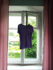 Purple T-shirt on a hanger drying hanging on a window frame. Drying clothes.