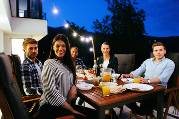 A group of young diverse people having dinner on the terrace of a modern house in the evening. Fun...