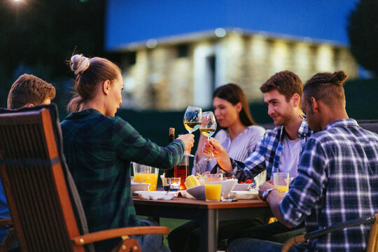 A group of young diverse people having dinner on the terrace of a modern house in the evening. Fun for friends and family. Celebration of holidays, weddings with barbecue