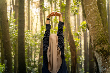 A woman in a black shirt and a scarf is stretching her arms in the forest