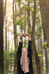 A woman in a black shirt and a scarf is stretching her arms in the forest