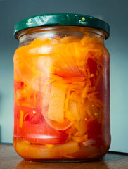 Colorful jar of homemade pickled vegetables with vibrant red and orange hues placed on a wooden...