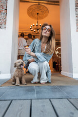Woman with a leash in hand and a happy dog sits near a warm café. City living, personal style, and pet love in a natural candid scene. Red-haired beautiful woman with dog