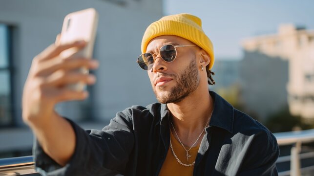 Young man wearing sunglasses takes a selfie on a sunny day while standing on a balcony in an urban environment
