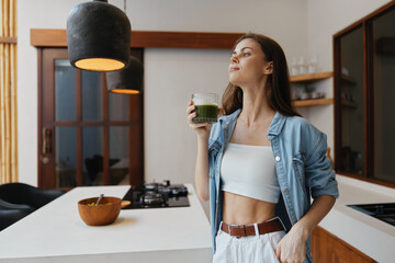 Young woman enjoying a healthy green smoothie in a modern kitchen, conveying freshness and wellness...