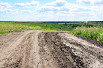 Muddy dirt road winding through a green landscape under a blue sky wallpaper