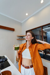 Young woman in orange shirt enjoying a healthy green smoothie in a modern kitchen, promoting...
