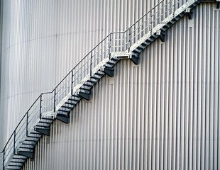 Metal staircase winding its way up the side of a corrugated metal silo, representing growth,...