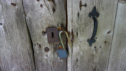 Rustic wooden door featuring weathered metal lock and handle, showcasing texture and natural aging....