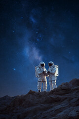 Two astronauts standing on rocky terrain under a starry night sky in outer space exploration.