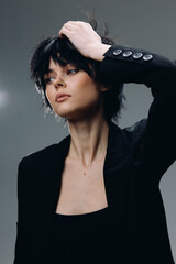 young woman with short black hair wearing black blazer posing thoughtfully with hand in hair...