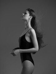 graceful woman in black swimsuit posing sideways with flowing hair against dark background in black...