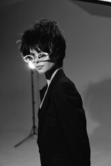 black and white woman wearing stylish sunglasses and dark blazer posing indoors with moody lighting...