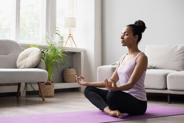 Woman meditating and practicing yoga at home. African american girl relaxing. Recreation, self...