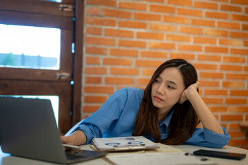 Bored businesswoman resting chin in hand while working on laptop