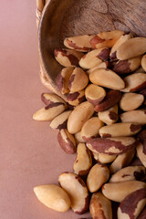 Brazil nuts, spilling out of a wooden plate on a beige mocha background with space for text....