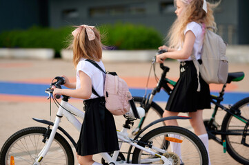 girls with bicycles near school wearing backpacks. school commute with eco-friendly transport....