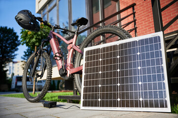 Pink electric mountain bike parked beside staircase, connected to small solar panel for charging....