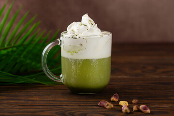 Pistachio green tea matcha latte in a glass with palm branch on wooden table.