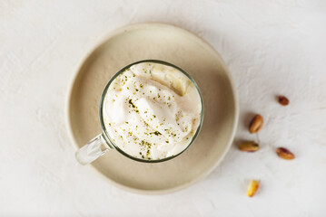 Pistachio matcha latte with whipped cream in a glass on a table. Top view.