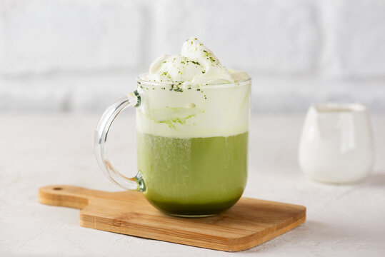 Cup of fresh green matcha latte tea with cream on wooden board