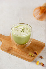 Pistachio matcha latte with milk in a glass on a wooden board. Vertical orientation.