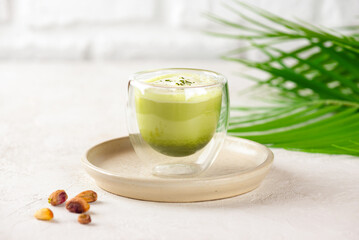 Pistachio green tea matcha latte with milk in a glass with palm branch on table.