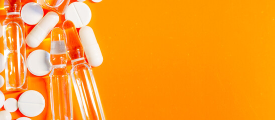 Medical supplies, including tablets, capsules, and ampoules, arranged on a bright orange...