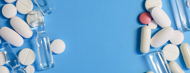 A rich blue background is framed by a scattering of white pills, capsules, and glass ampoules along...