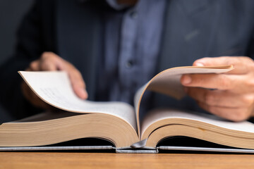 Close-up of hands flipping pages of an open book on wooden desk, symbolizing research, study,...