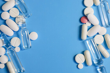 On a light blue background, white and red pills of various shapes are arranged, along with glass...