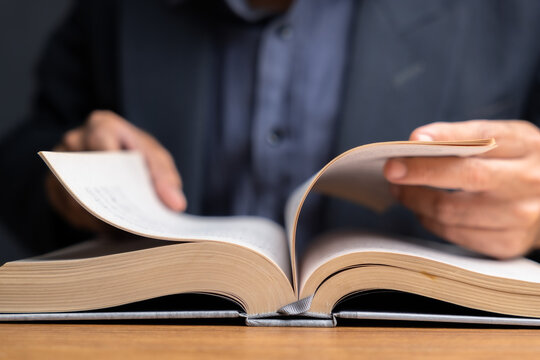 Close-up of hands flipping pages of an open book on wooden desk, symbolizing research, study, reading, and finding references or information for work, education, or business
