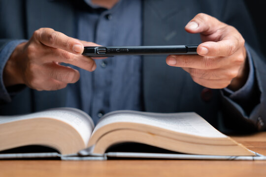 Close-up of businessman’s hands using smartphone to capture and convert book text with OCR technology. Concept of digitizing information, paperless work, and modern research