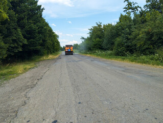 Dense green trees line both sides of the road, forming a picturesque natural corridor. In the...